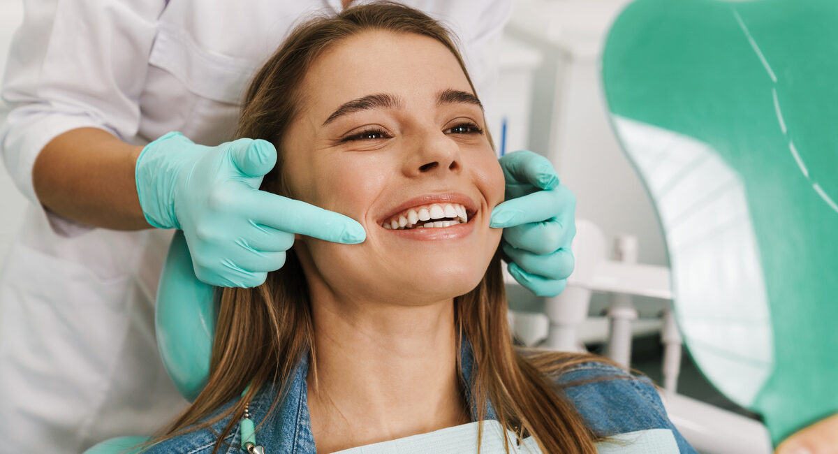 European young woman smiling while looking at mirror in dental c