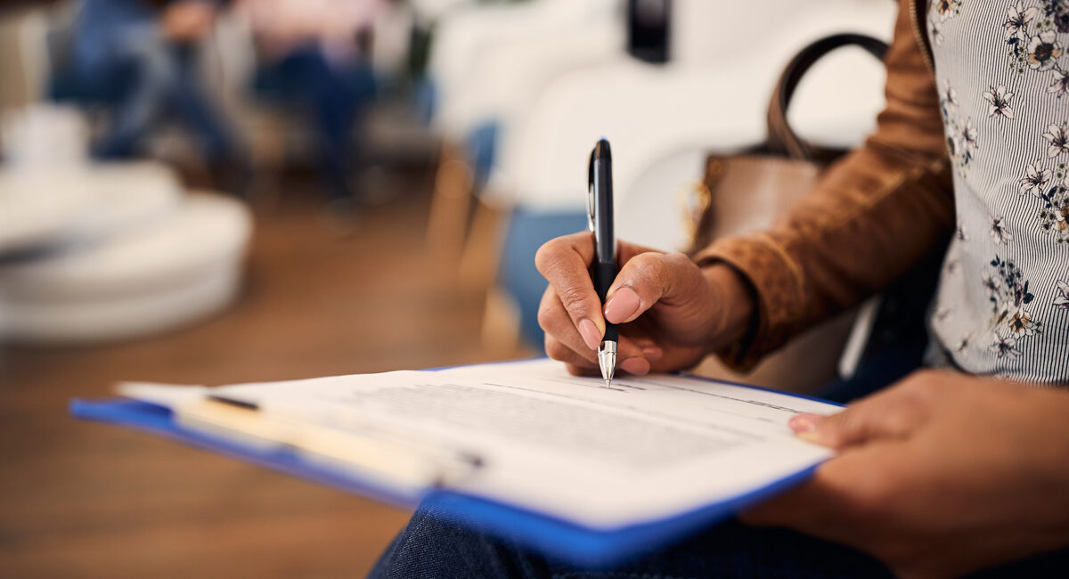 Close up of black woman writing filling medical documents in waiting room at clinic.